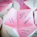 The bride and groom made custom pink and white "cootie catchers" for their ceremony program, full of facts about the groomsmen and bridesmaid. They wanted their guests to become better acquainted with their wedding party during their ceremony.