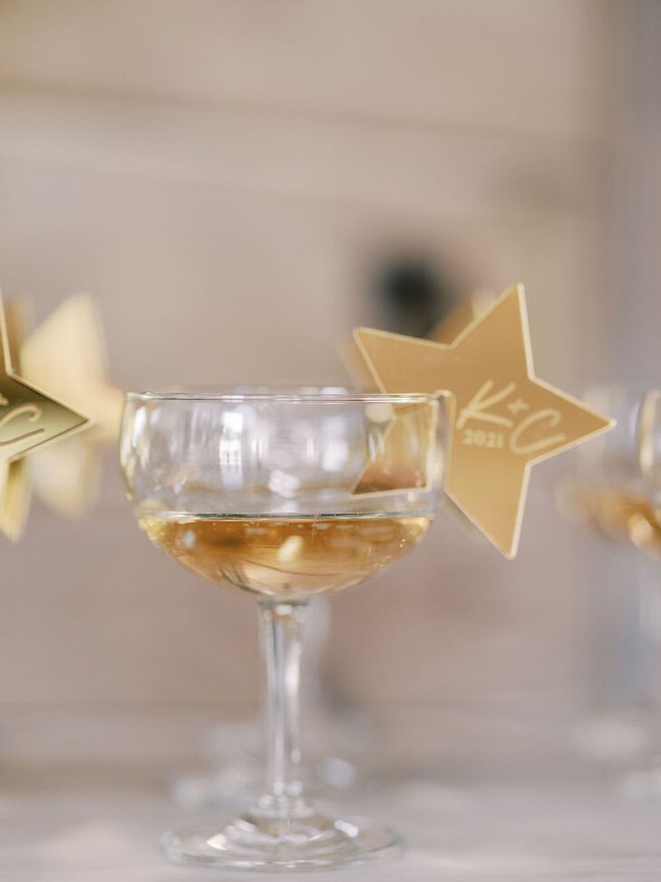 A chic couple glass at a rehearsal dinner bar with Champagne and a custom gold star drink marker to represent the 4th of July wedding weekend.