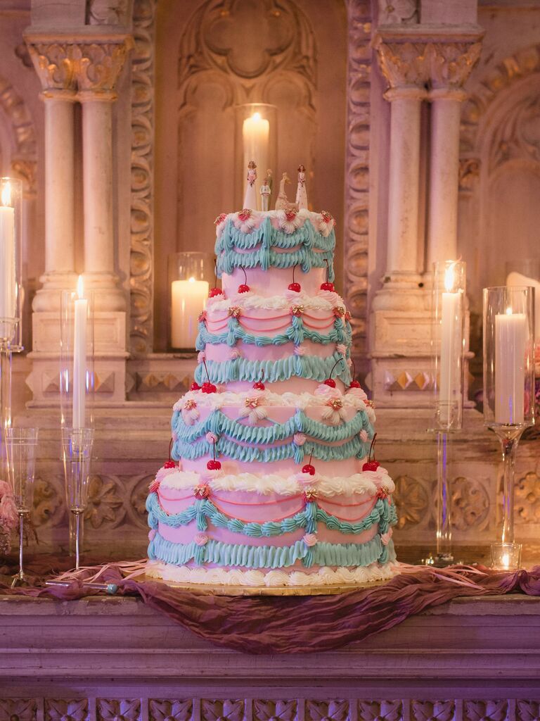 four tier vintage style wedding cake with pink buttercream, blue and white piping, and red cherries