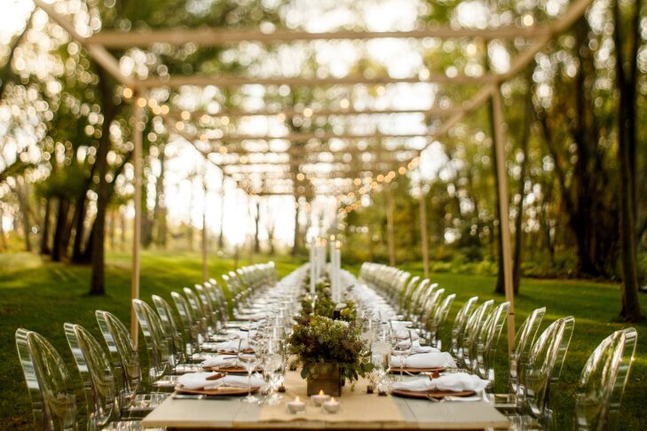 Dave and Chad built their own sixty-foot, wood reception table and it's accompanying trellis from which they draped a series of string lights for their dusk wedding. They pulled the clear ghost chairs from the ceremony to sit at the modern tablescape.